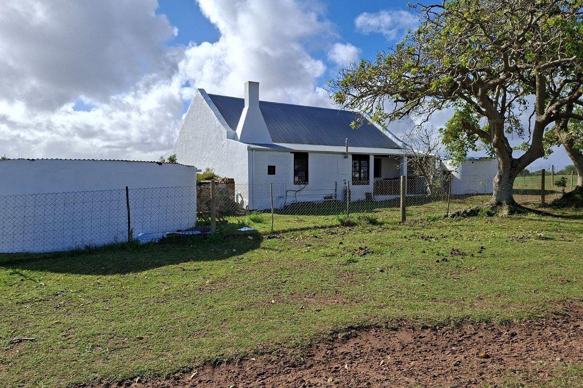 A view of the rear exterior of a traditional white farmhouse with a pitched metal roof, set within a rural landscape.
