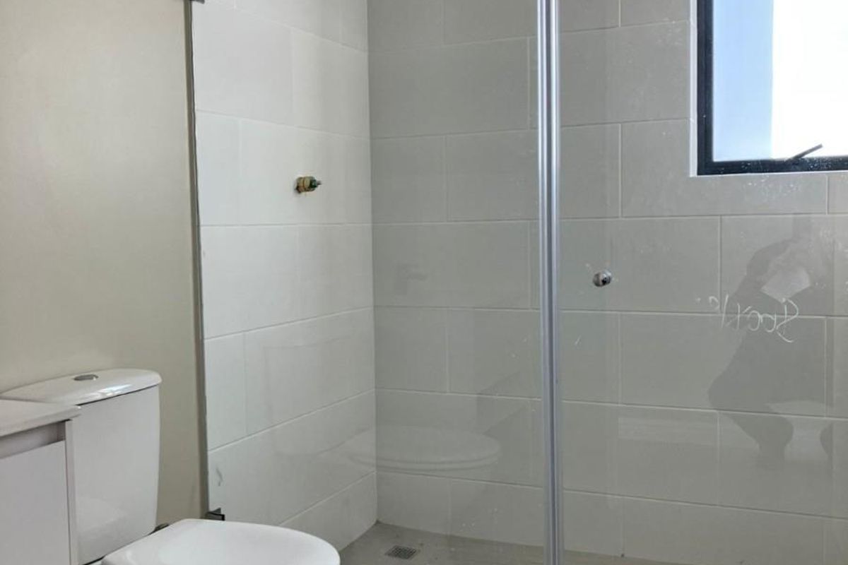 A modern bathroom featuring a walk-in glass shower enclosure with white wall tiling, a contemporary toilet, and a window for natural light.