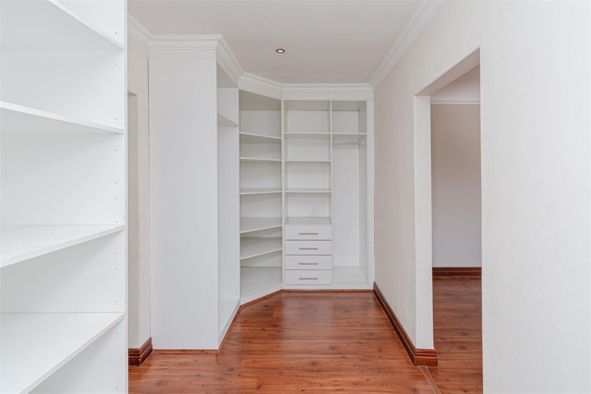 A clean, empty walk-in closet or dressing area featuring extensive built-in white cabinetry, laminate flooring, and modern recessed lighting.