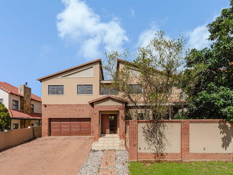 Front elevation of a multi-story house featuring a brick facade, double garage, and a paved driveway with a gated entrance.