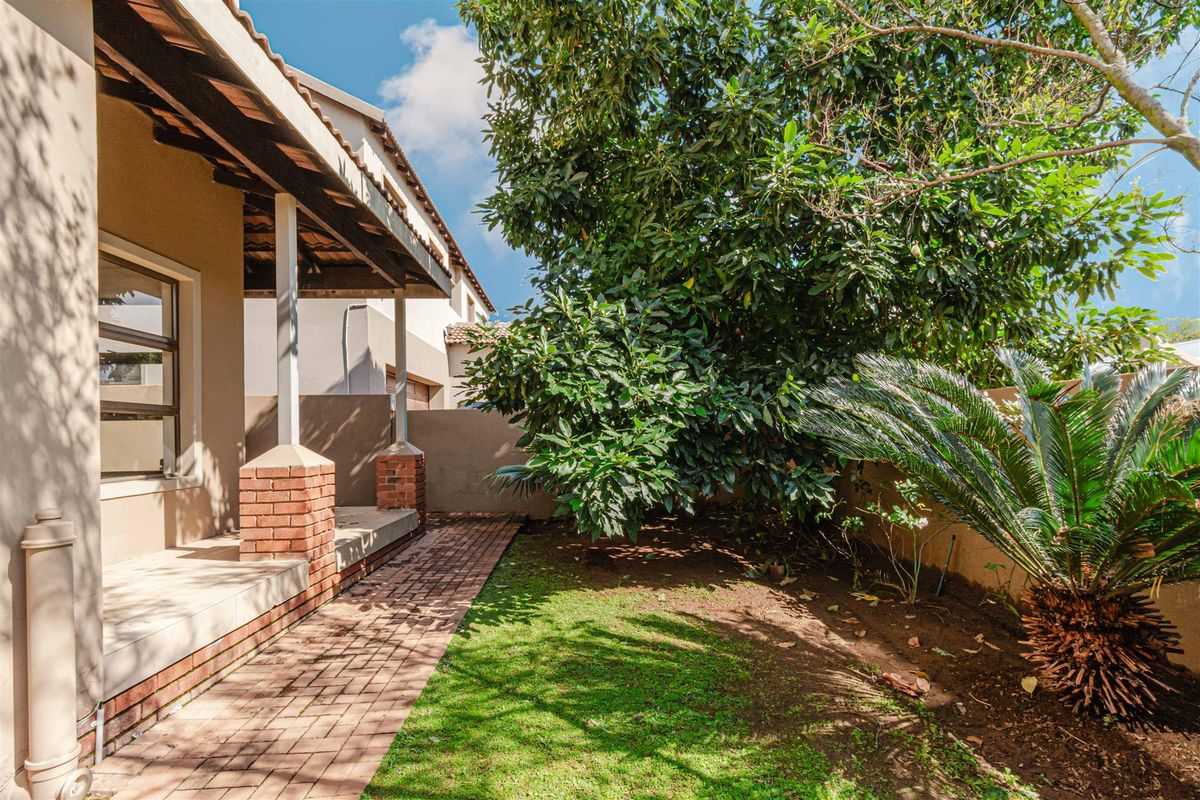 A private rear garden featuring a brick-paved walkway, a covered patio area with brick pillars, and established greenery along the boundary wall.