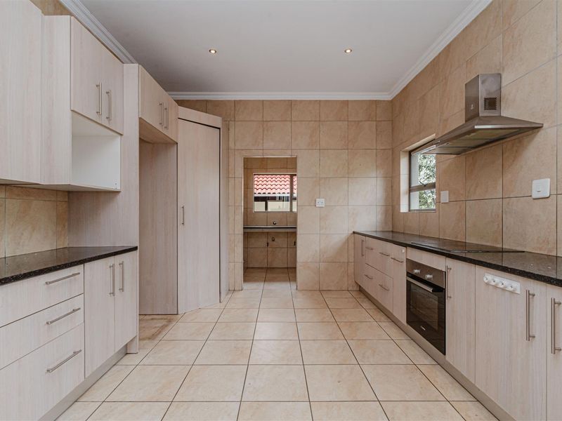 A clean, functional kitchen featuring light wood-finish cabinetry, granite countertops, built-in oven, extractor fan, and neutral ceramic tiling throughout.