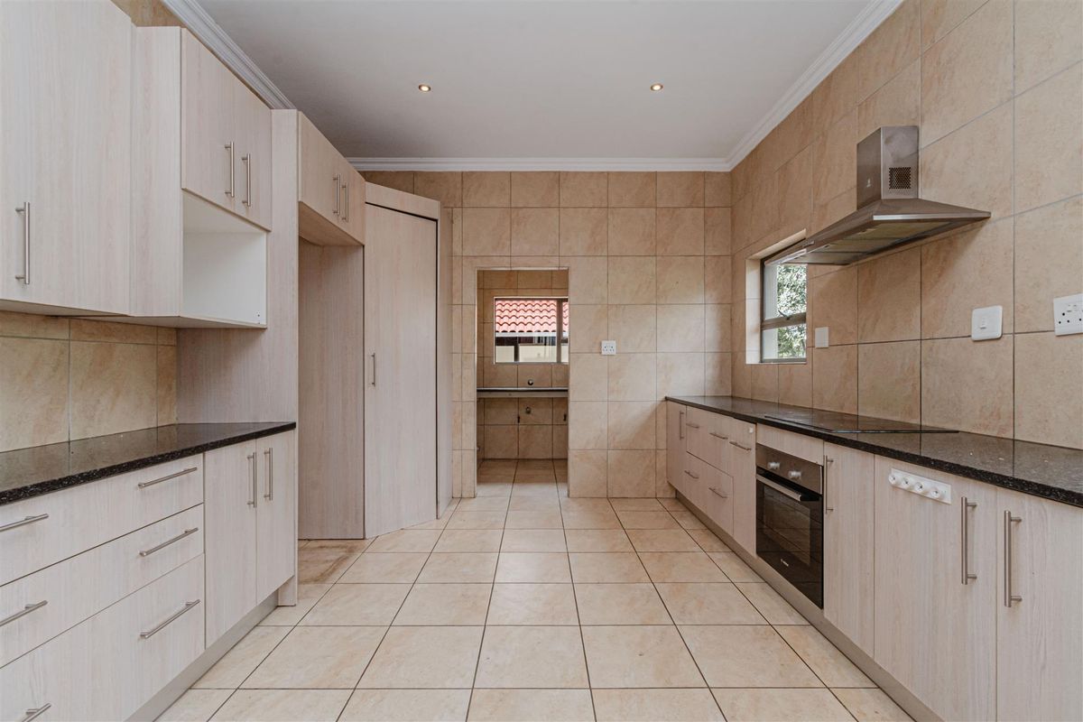 A clean, functional kitchen featuring light wood-finish cabinetry, granite countertops, built-in oven, extractor fan, and neutral ceramic tiling throughout.