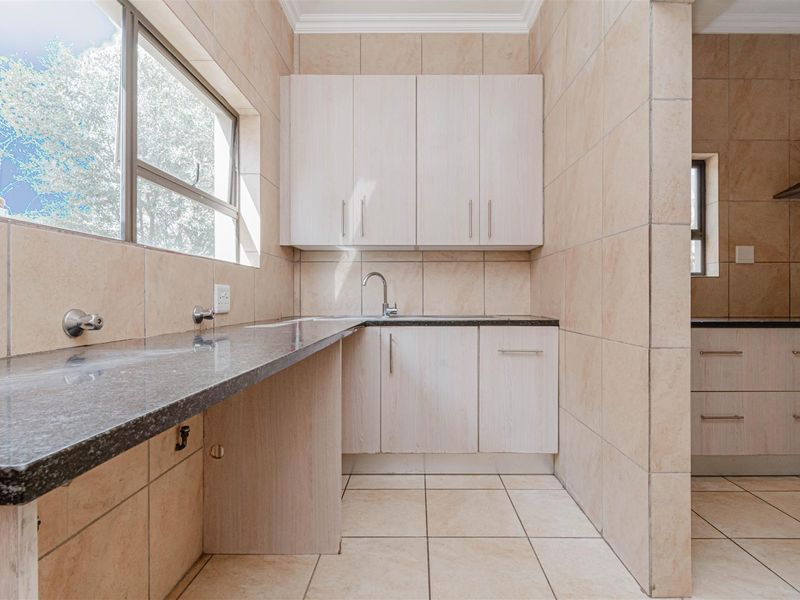 A clean and functional scullery area featuring granite countertops, ample built-in cabinetry, and tiled finishes, providing a dedicated space for food preparation and cleaning.
