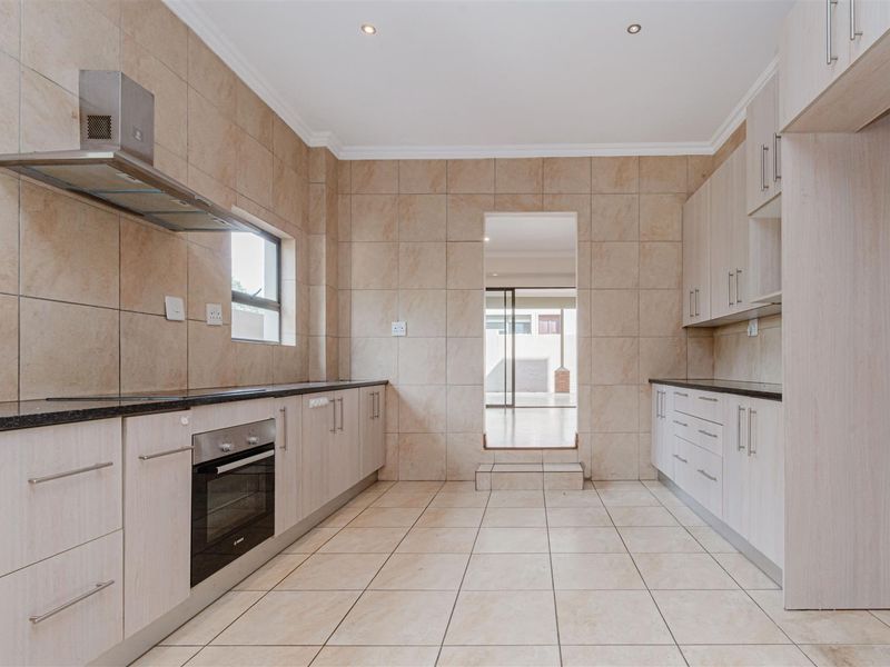 A clean, modern kitchen featuring light wood-finish cabinetry, granite countertops, built-in oven, extractor fan, and neutral ceramic tiling throughout.