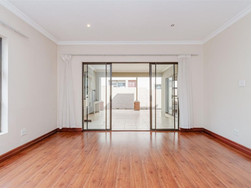 A bright, empty living room featuring laminate flooring, recessed lighting, and large sliding glass doors that open onto a covered patio area.