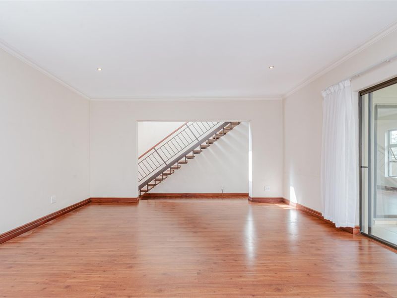 Spacious, light-filled living area featuring warm-toned laminate flooring, recessed lighting, and a feature staircase with a modern metal railing.