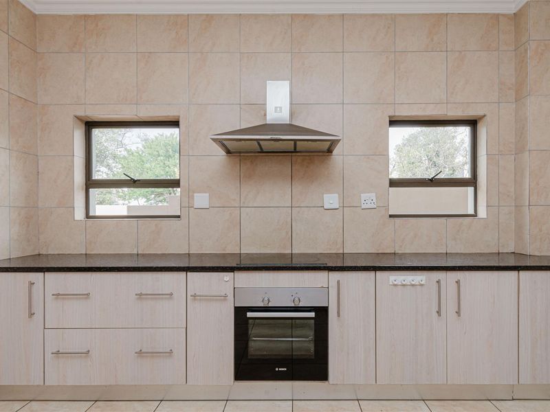 A clean, functional kitchen featuring light wood-finish cabinetry, dark granite countertops, a built-in oven, and a stainless steel extractor fan.
