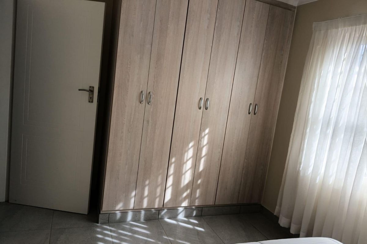 A bright bedroom featuring neutral-toned built-in cupboards, tiled flooring, and natural light filtering through the window.