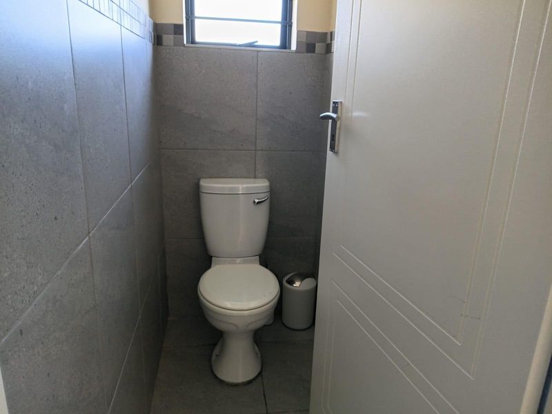 A compact, modern guest toilet featuring neutral grey wall and floor tiles and a window for natural ventilation.