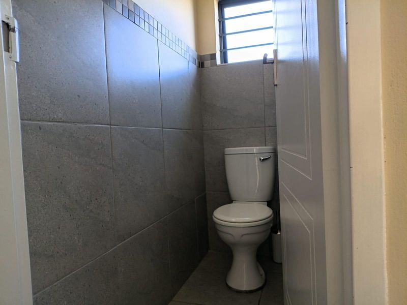 A compact, functional bathroom featuring modern grey wall tiles, tiled flooring, and a standard white toilet.
