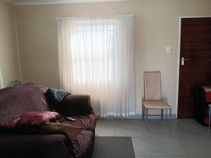 A living room area featuring tiled flooring, a wooden door, and a window fitted with security bars.