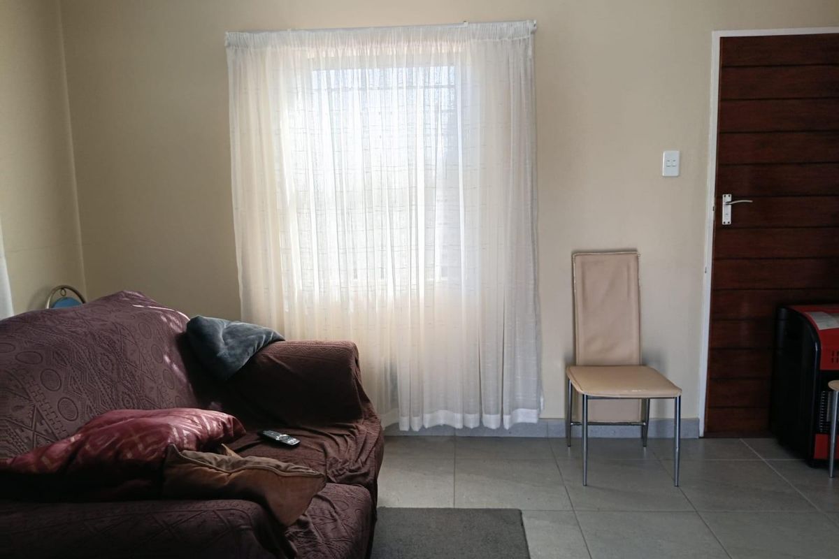 A living room area featuring tiled flooring, a wooden door, and a window fitted with security bars.