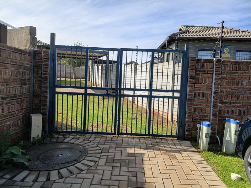 A secure rear entrance featuring a metal gate, brick boundary walls, and paved access leading to a private garden area.