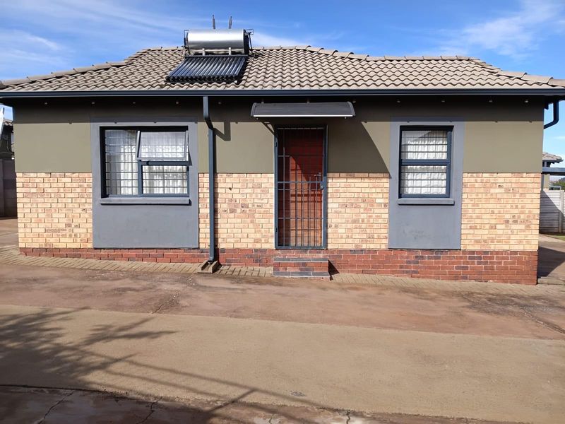 Front elevation of a single-story house featuring a facebrick facade, tiled roof, solar water heater, and secure entrance with burglar bars.