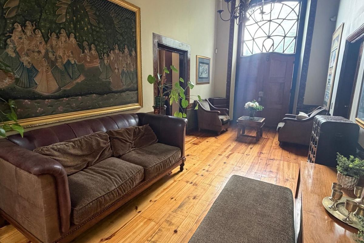 Spacious living area featuring polished hardwood flooring, a grand arched timber entrance door with decorative fanlight, and a classic wrought iron chandelier.