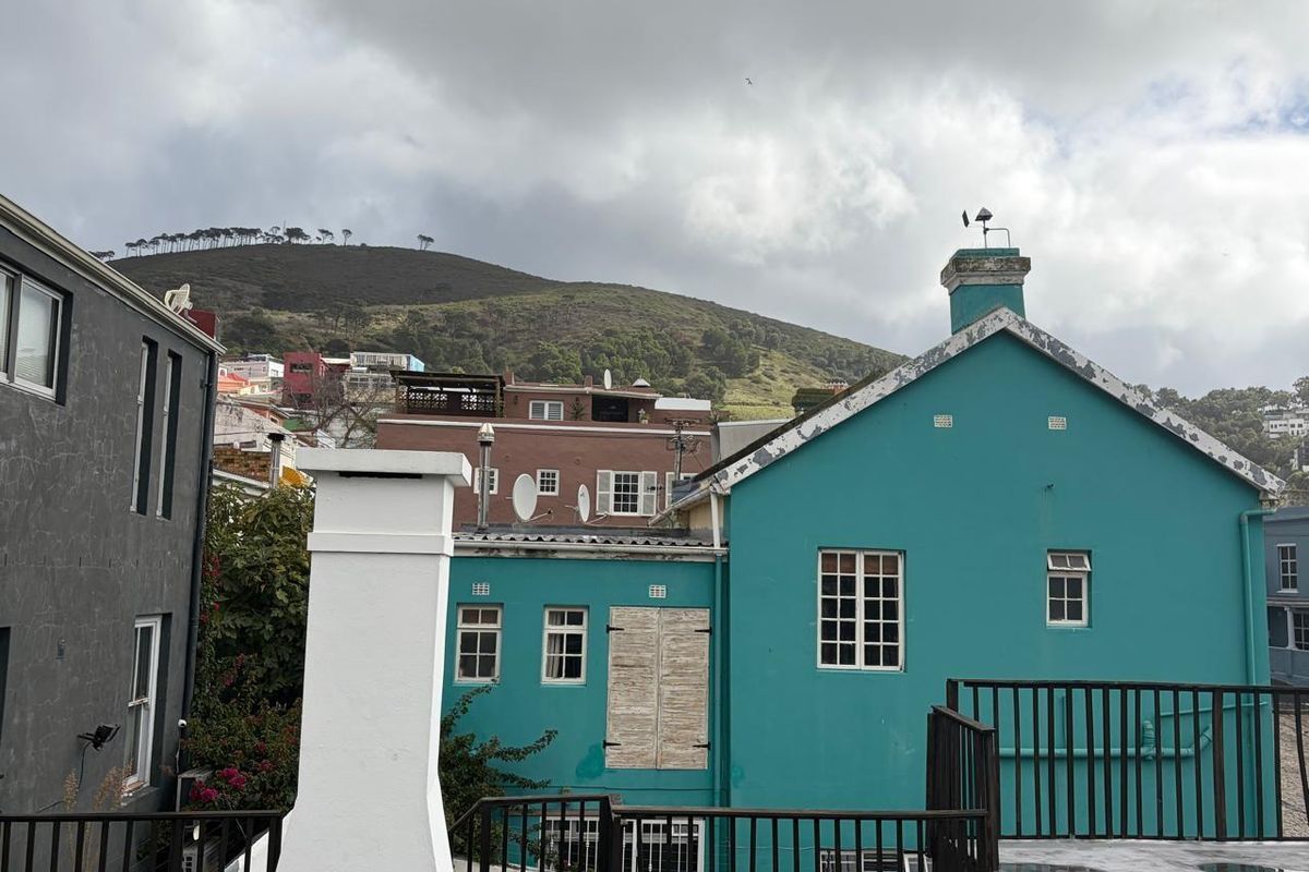 Rear exterior view of a teal-colored building featuring a chimney, metal safety railings, and mountain views in the background.