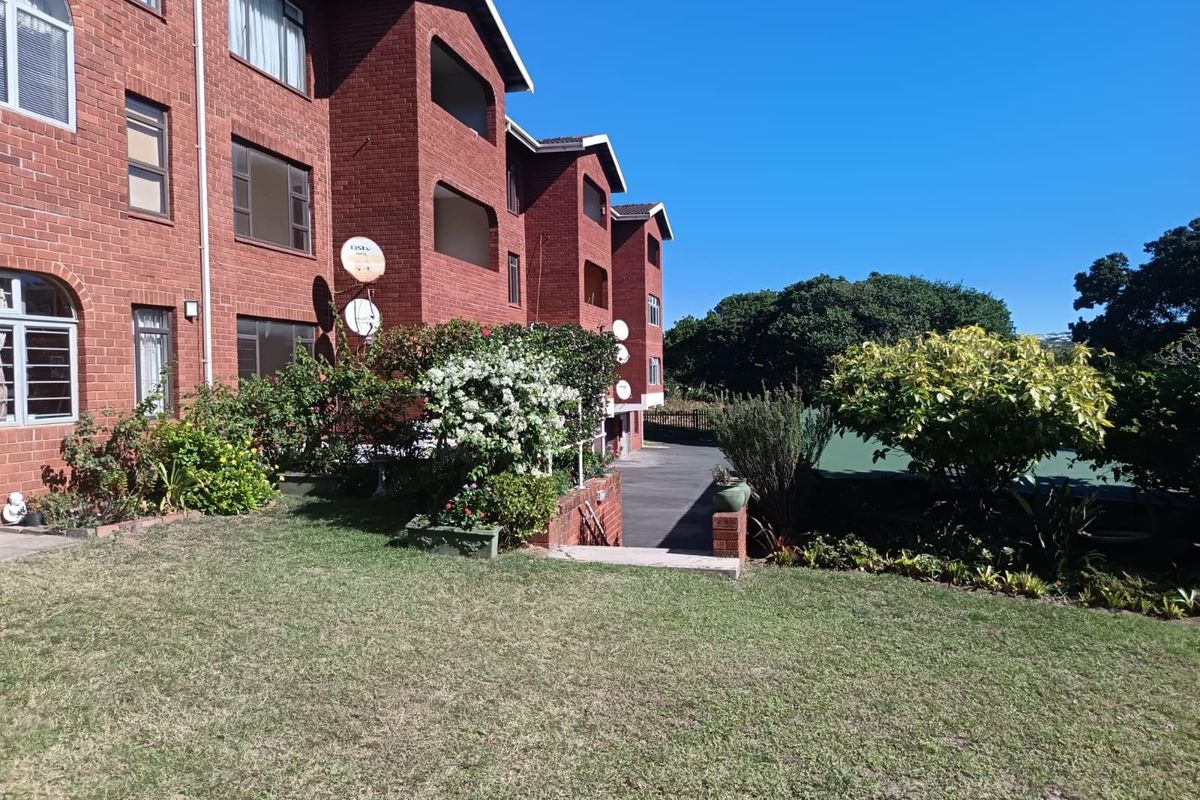 A view of the rear face brick apartment building facade featuring private balconies, a well-maintained lawn, and established garden landscaping.