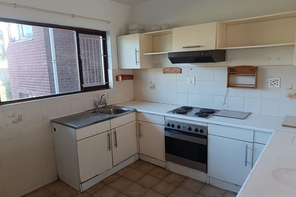 A functional kitchen featuring built-in cabinetry, a stainless steel sink, and an integrated oven with hob, offering a blank canvas for renovation.