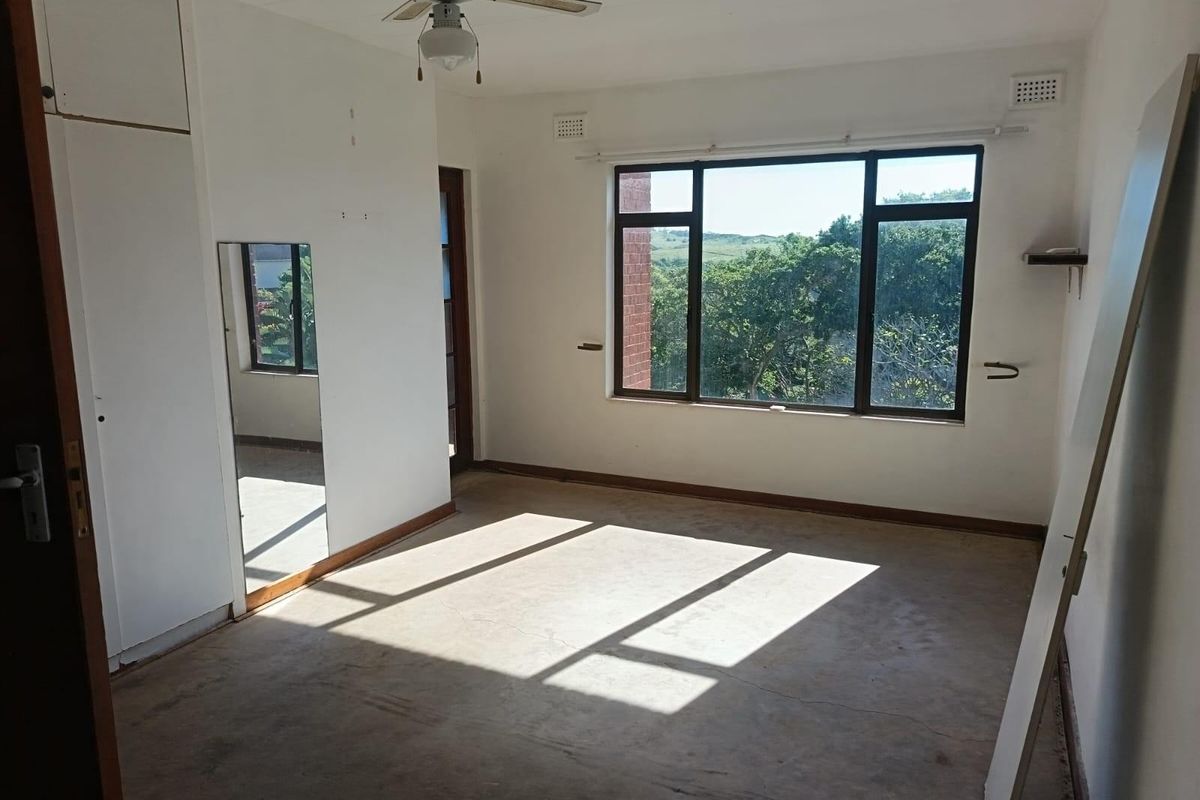 An empty bedroom featuring a ceiling fan, built-in cupboard, and large windows with natural light, ready for renovation or new flooring installation.