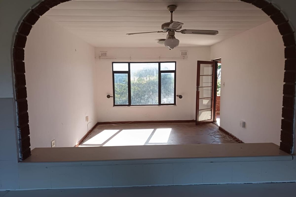An empty living room featuring a distinctive brick archway, ceiling fan, and access to an outdoor area through a timber-framed door.
