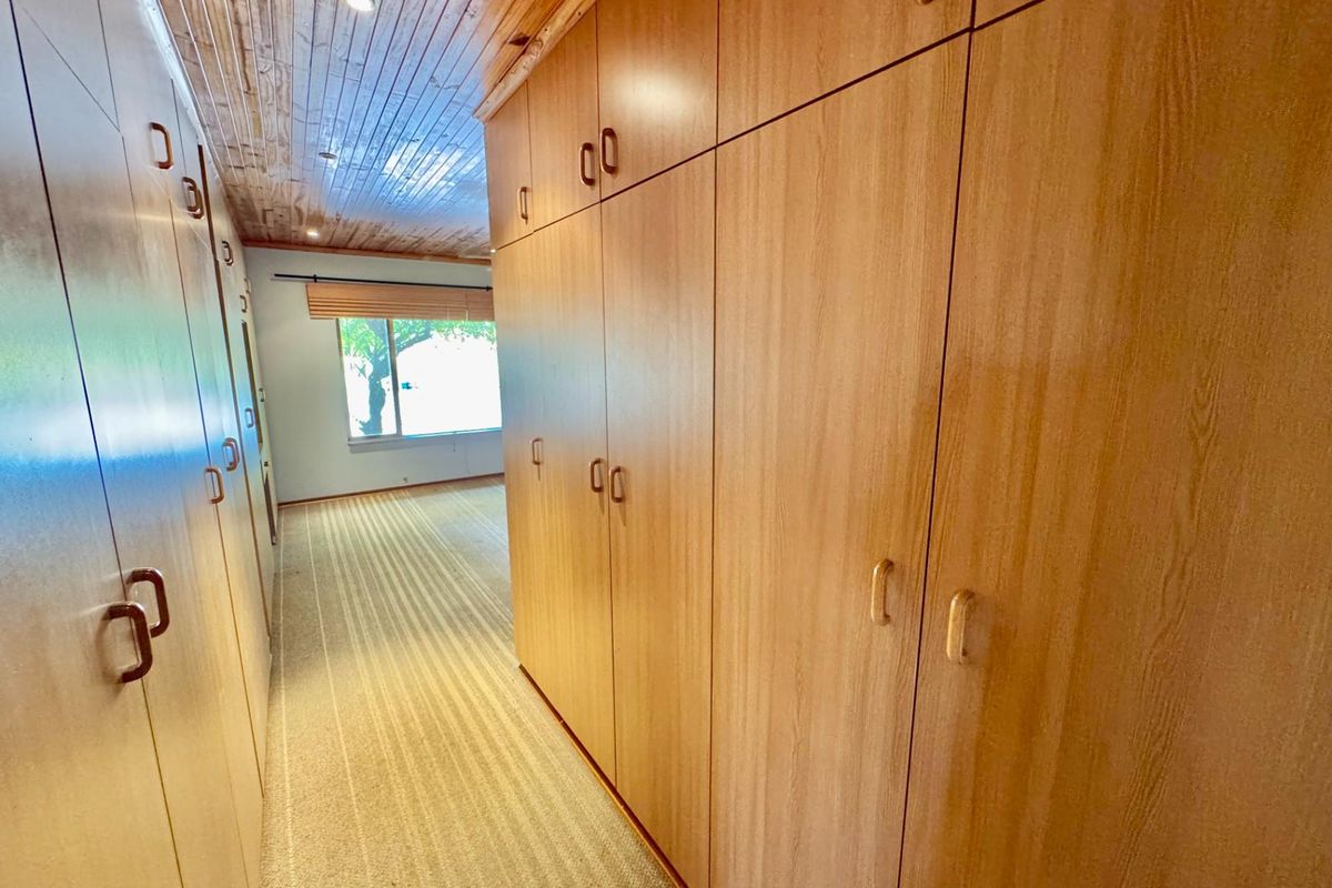 A bedroom featuring extensive built-in wooden cabinetry, a wood-paneled ceiling, and carpeted flooring with a window providing natural light.