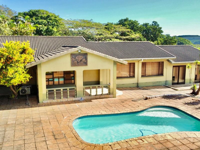 Rear view of the house featuring a covered patio, tiled pool area, and established garden surroundings.