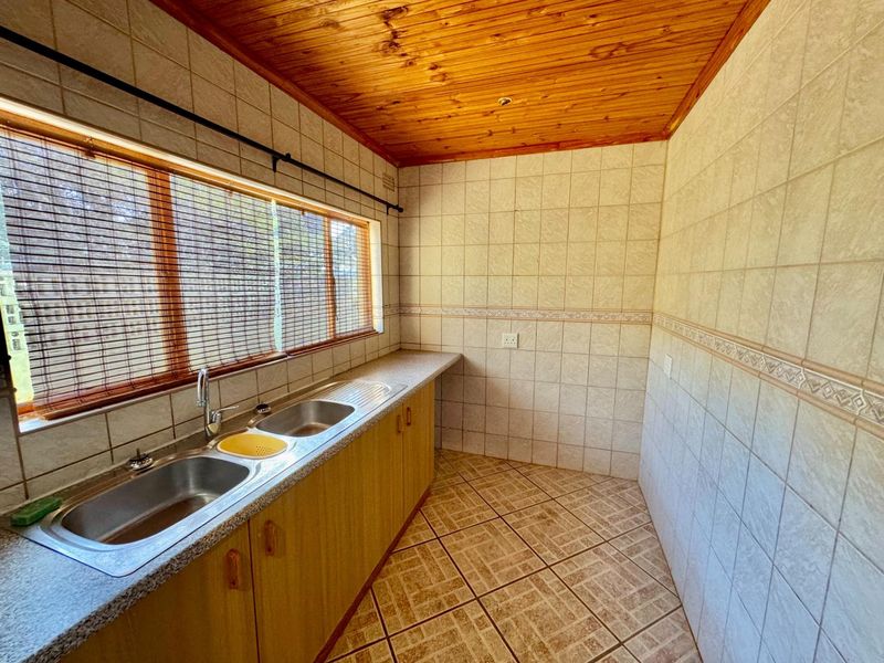 A functional scullery area featuring a double stainless steel sink, laminate countertops, tiled walls, and a timber-paneled ceiling.