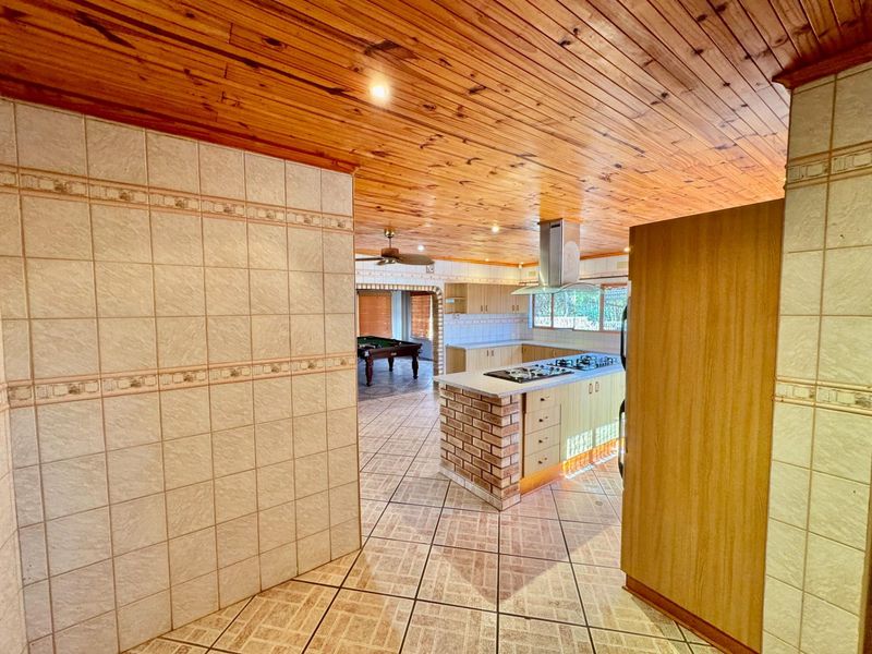 Open plan kitchen featuring a central island with built-in gas hob, extractor fan, and tiled flooring, flowing into an adjacent living area.