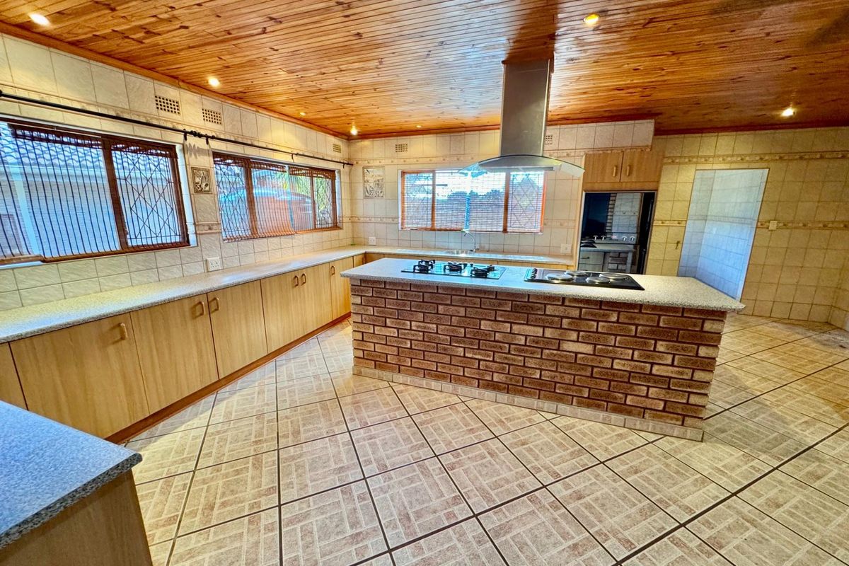 Spacious kitchen featuring a central brick island with built-in gas hob, extractor fan, extensive laminate cabinetry, and tiled flooring under a timber-clad ceiling.