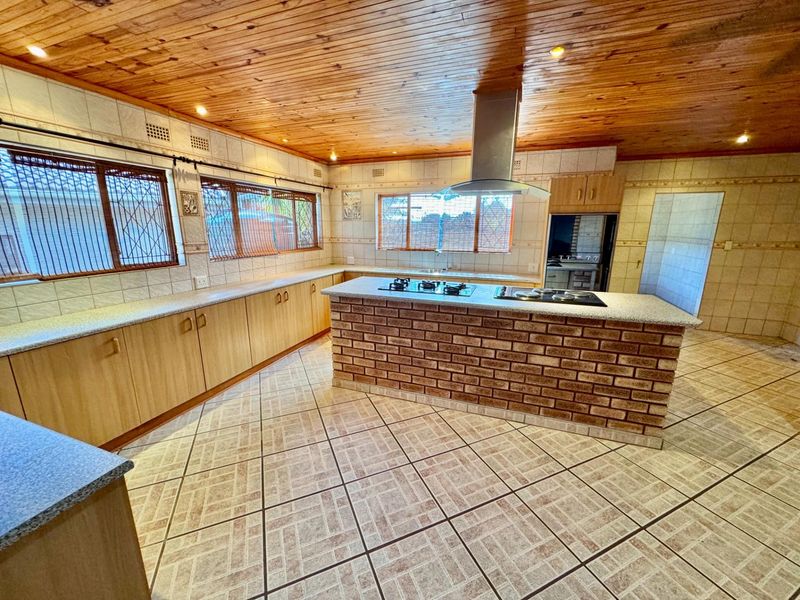 Spacious kitchen featuring a central brick island with built-in gas hob, extractor fan, extensive laminate cabinetry, and tiled flooring under a timber-clad ceiling.