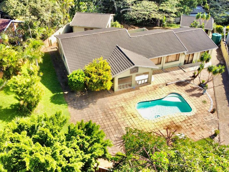 Aerial view of a residential property featuring a tiled roof house, a swimming pool, paved patio area, and established garden surroundings.