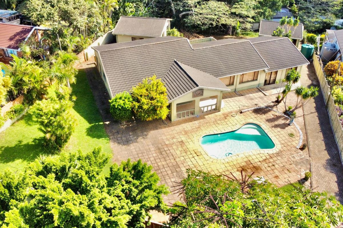 Aerial view of a residential property featuring a tiled roof house, a swimming pool, paved patio area, and established garden surroundings.