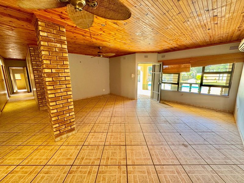Spacious living area featuring exposed brick columns, timber-clad ceiling, tiled flooring, and direct access to the outdoor pool area.