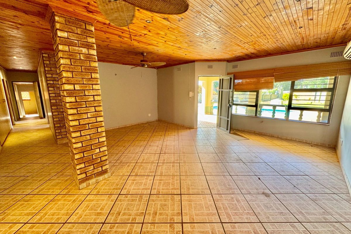 Spacious living area featuring exposed brick columns, timber-clad ceiling, tiled flooring, and direct access to the outdoor pool area.