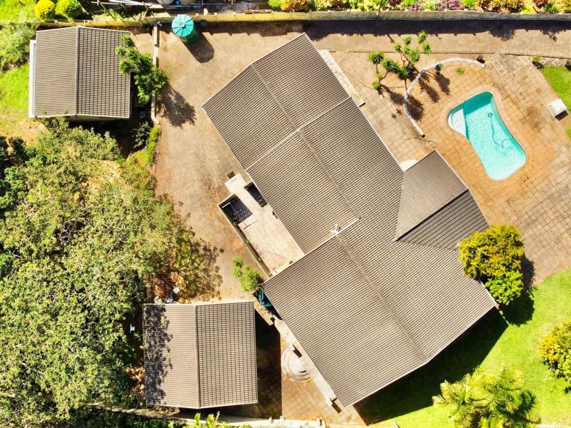 Aerial view of the property featuring a tiled roof house, swimming pool, paved driveway, and surrounding garden areas.