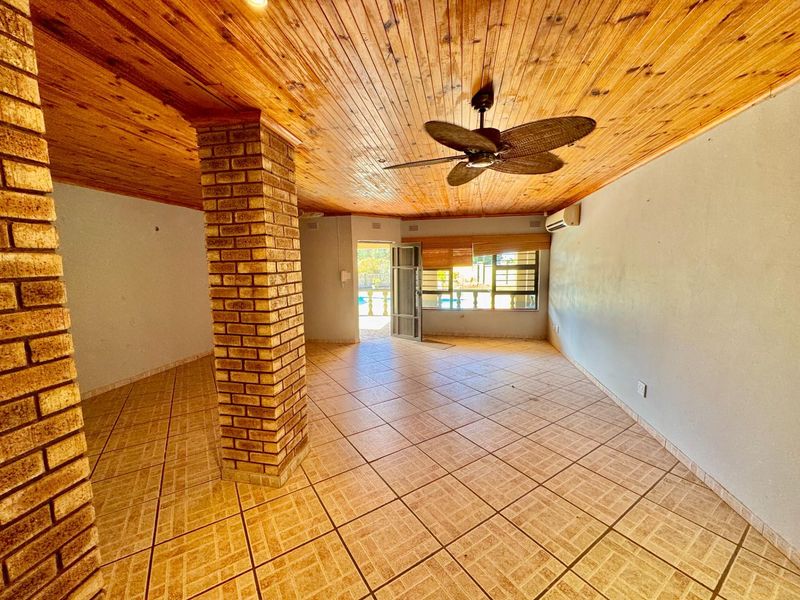 Spacious living area featuring a distinctive exposed brick pillar, timber-clad ceiling, tiled flooring, and direct access to the outdoor pool area.