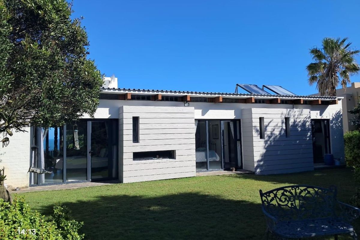 Rear exterior view of the property featuring modern horizontal cladding, large glass sliding doors, and roof-mounted solar water heating panels overlooking a garden.