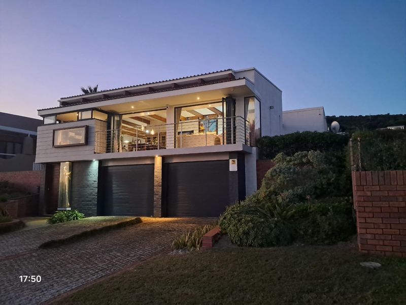 Modern double-story residence featuring a paved driveway, double garage, and an elevated balcony with large glass sliding doors overlooking the surrounding area.