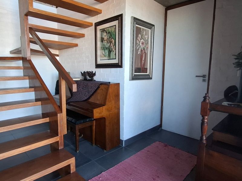 An inviting entrance hall featuring a striking open-tread timber staircase, tiled flooring, and a clean, minimalist aesthetic.