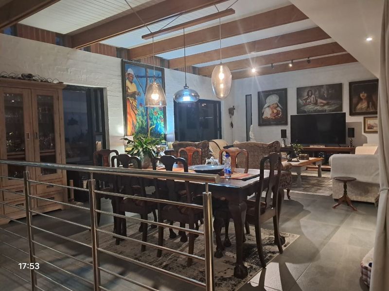 Spacious open-plan living and dining area featuring exposed timber ceiling beams, tiled flooring, and a modern stainless steel balustrade.
