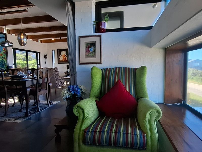 Open-plan living area featuring exposed timber ceiling beams, large windows with coastal views, and a bright, airy atmosphere.