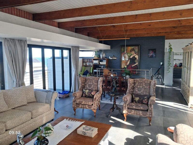 Spacious open-plan living and dining area featuring exposed timber ceiling beams, large sliding glass doors, and dark tiled flooring.