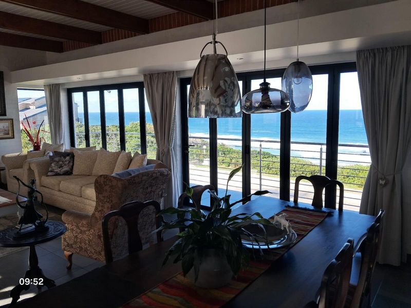 Open-plan living and dining area featuring exposed timber ceiling beams and large black-framed sliding doors opening to a scenic ocean view.