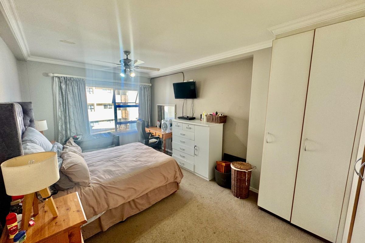 A spacious bedroom featuring built-in wardrobes, a ceiling fan, and large windows allowing for natural light.