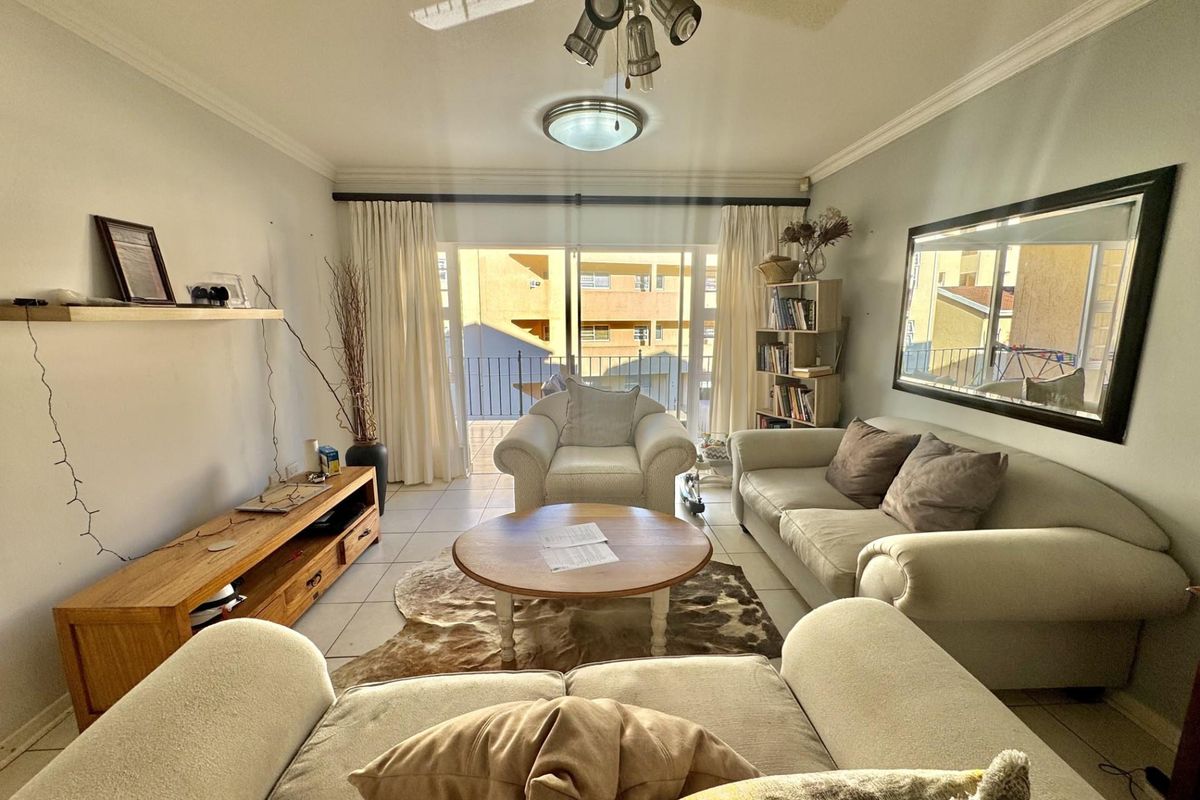 A comfortable living room featuring tiled flooring, crown molding, a ceiling fan, and large sliding glass doors leading to a private balcony.