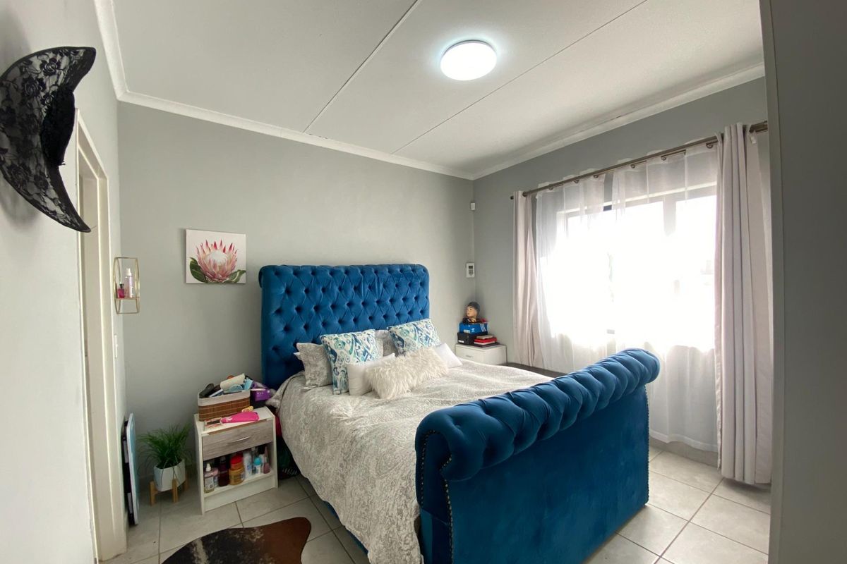 A well-maintained bedroom featuring neutral wall tones, tiled flooring, and a large window with curtain rails, providing ample natural light.