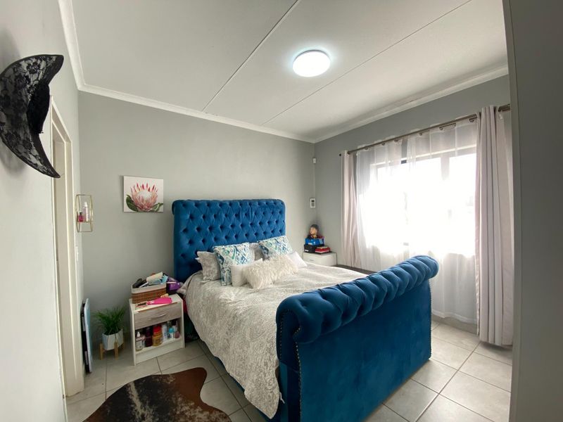 A well-maintained bedroom featuring neutral wall tones, tiled flooring, and a large window with curtain rails, providing ample natural light.