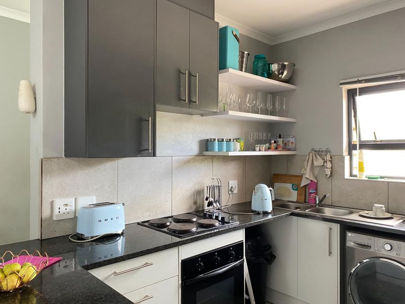 A compact kitchen featuring dark granite countertops, a built-in electric hob and oven, stainless steel sink, and a mix of cabinetry and open shelving.