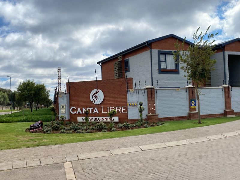 Front entrance view of the Canta Libre townhouse complex, featuring a brick boundary wall, electric fencing, and well-maintained landscaped garden.